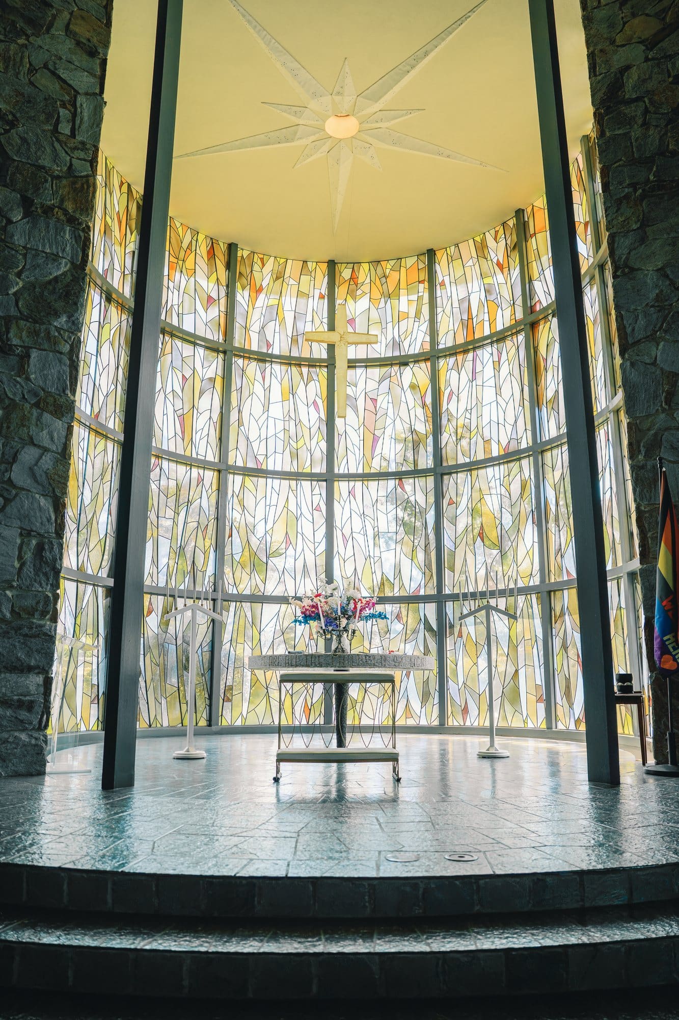 Tall stained glass surrounds the altar beneath a suspended cross at The Santa Anita Church in Arcadia, California.